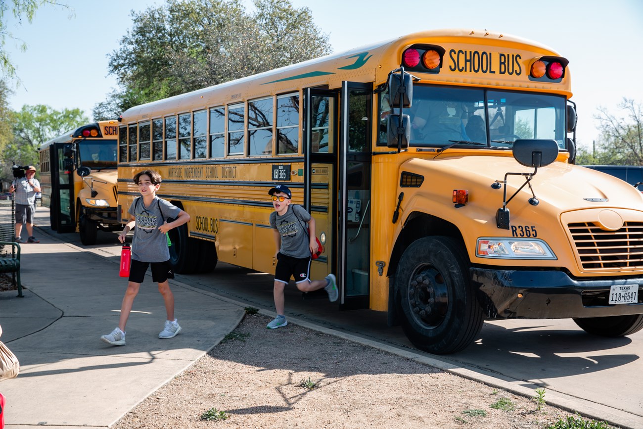 Yellow school bus with kids running off of it into the sidewalk
