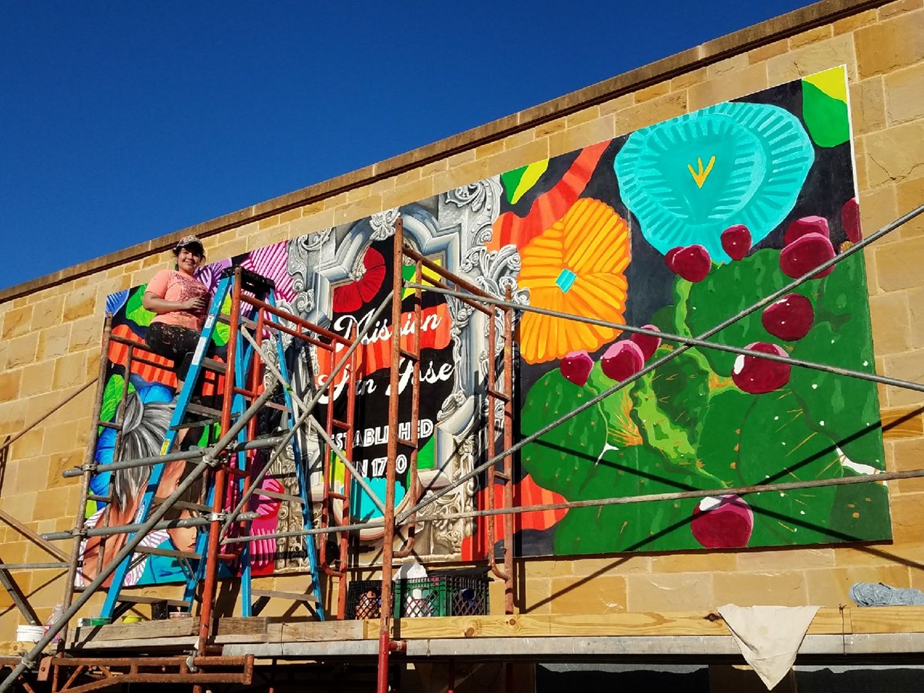 Artist Sandra Gonzalez paints a colorful mural on the exterior of the Visitor Center.