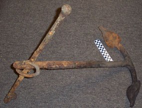 A rusty boat anchor with ring and t-bar on top