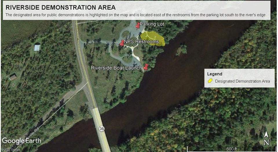 Aerial map image of a green forest with a river flowing through the middle. White lettering next to red thumbtacks over the tops of green trees.