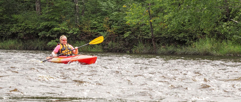 A woman paddles a kayak in moving water.