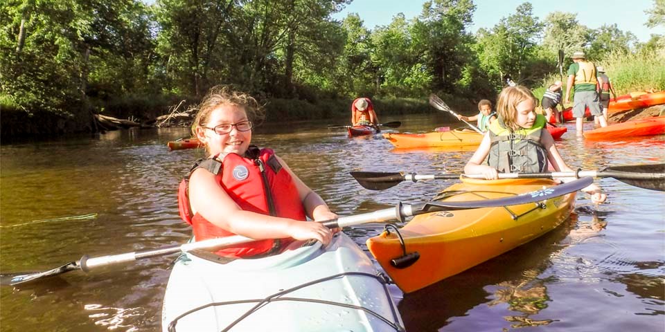Young paddlers in kayaks start a trip on a river.