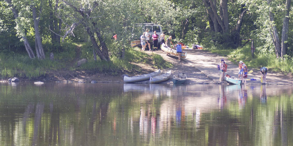 A group of people unload canoes at a river landing.
