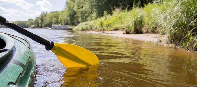 A yellow paddle dips into a river from the side of a kayak.