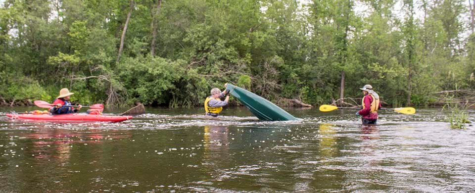 A paddler turns a flipped kayak over in a river while others watch.
