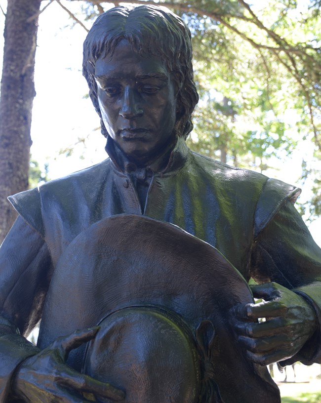 A bronze statue depicting Samuel de Champlain praying.