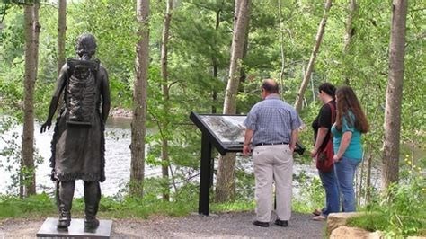 Three people standing in a wooded area with their backs to the camera reading a panel.