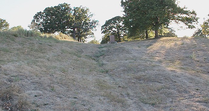 steep rut with shrubby grass, a stone plaque, and trees