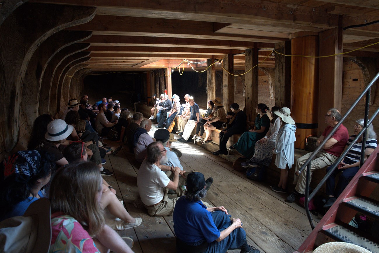 People gathered in the lower hold of a ship singing and playing instruments