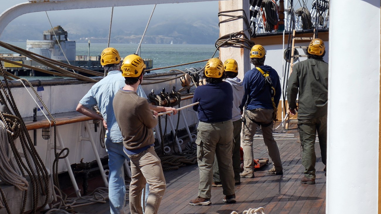 Volunteers rigging crew wearing helmets working aboard a ship
