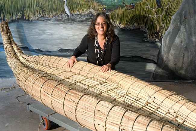 a woman poses with a reconstructed tule reed boat