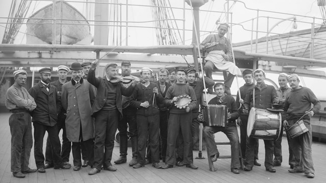 a group of men aboard a ship, several with musical instruments