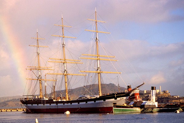 A three-masted historic ship moored at a pier.