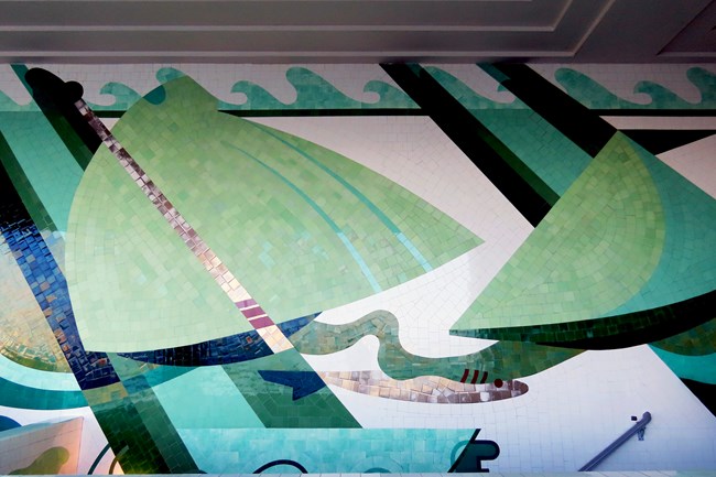 a wall of mosaic tile murals with abstract green, gray and white shapes resembling ships.