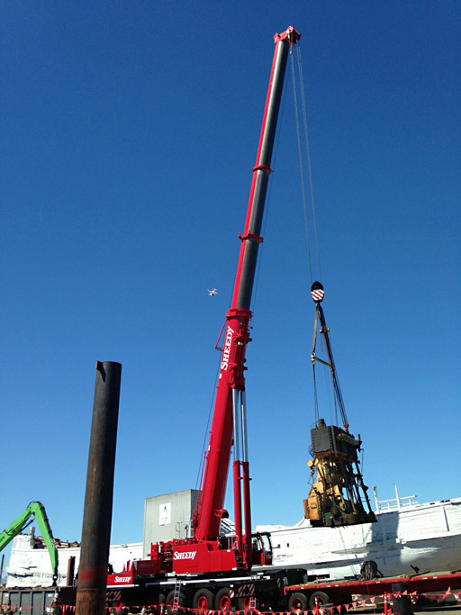 A red crane lifting a large engine off a ship.