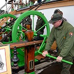 A park ranger turning the handle of a pump on the deck of Balclutha.