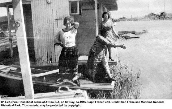 A black and white photo of three women standing on the deck of a houseboat.