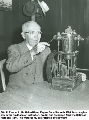 Otto Fischer seated at a desk with an 1885 prototype of the Regan Vapor engine sitting on the tabletop.