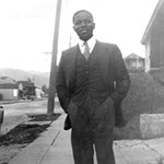 A man standing on a sidewalk wearing a three- piece suit.