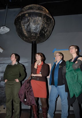 Four people standing near a large sphere atop a pole.