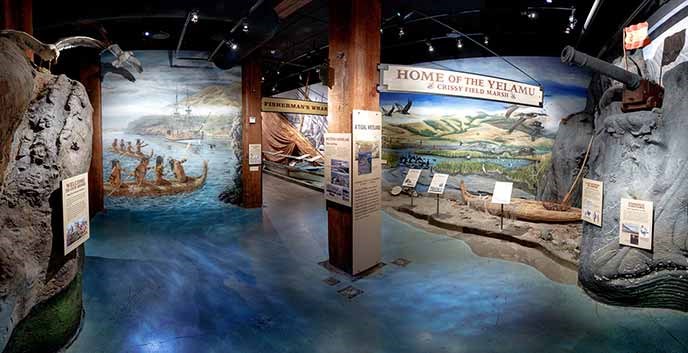 The entrance to an exhibit in the visitor center with blue-colored flooring and murals painted on the walls.