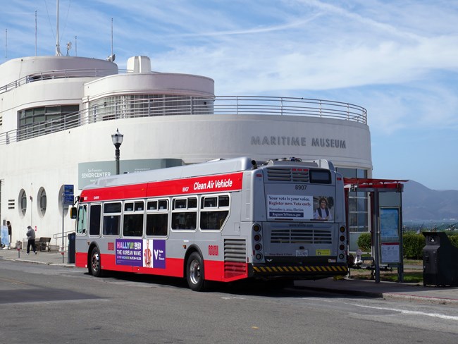 a SF city bus stops in front of the Maritime Museum