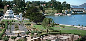 A view of the Aquatic Park Historic District which includes a lawn area, flowerbeds, benches, a promenade along the waterfront, and a spectacular view of the Aquatic Park lagoon and San Francisco Bay.