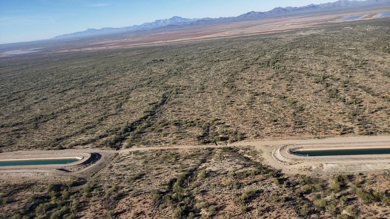 Aerial view of a strip of natural desert land interrupting a canal to form a connection with the greater desert landscape.