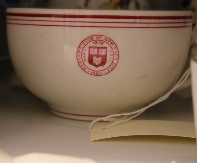A white coffee cup with red seal of the New York Harvard Club