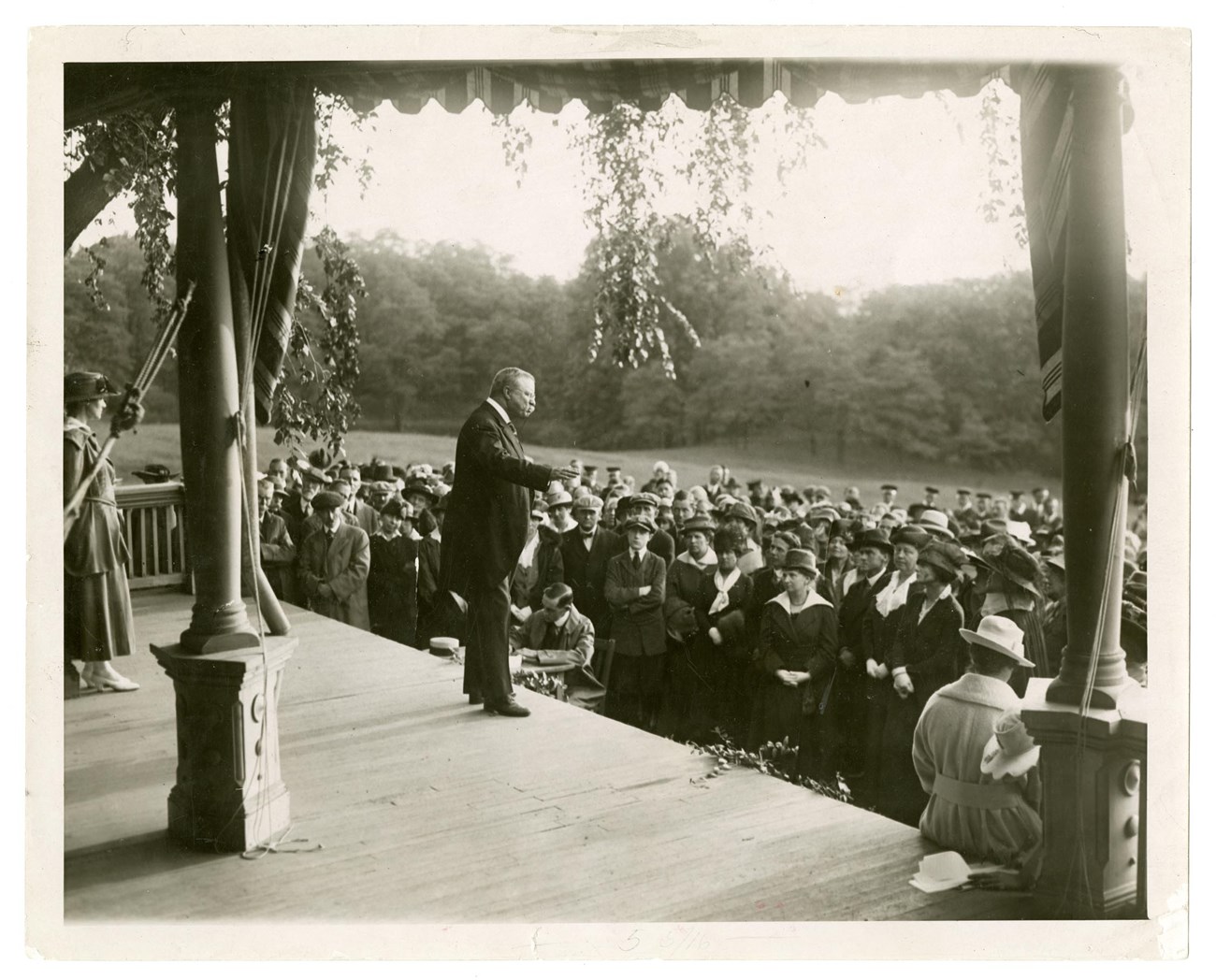 Theodore Roosevelt stands on the porch of Sagamore Hill speaking to a crowd of woman suffragists who stand before him on the lawn. NPS Photo