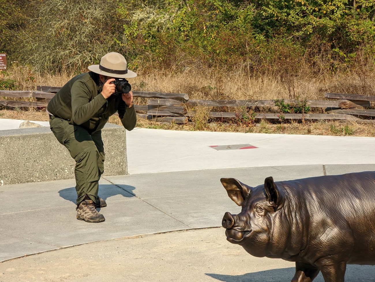 photo of a man in park ranger uniform taking a picture of a pig statue
