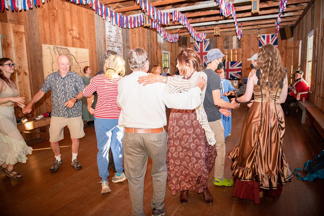 photo of numerous people in period dress dancing enthusiastically in a picturesque 19th century building