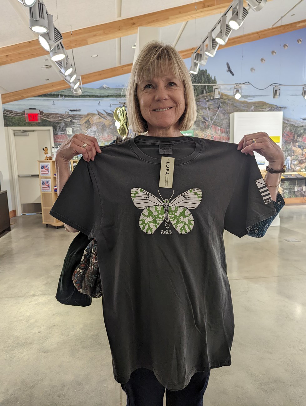 A woman proudly displays a tee shirt featuring an island marble butterfly