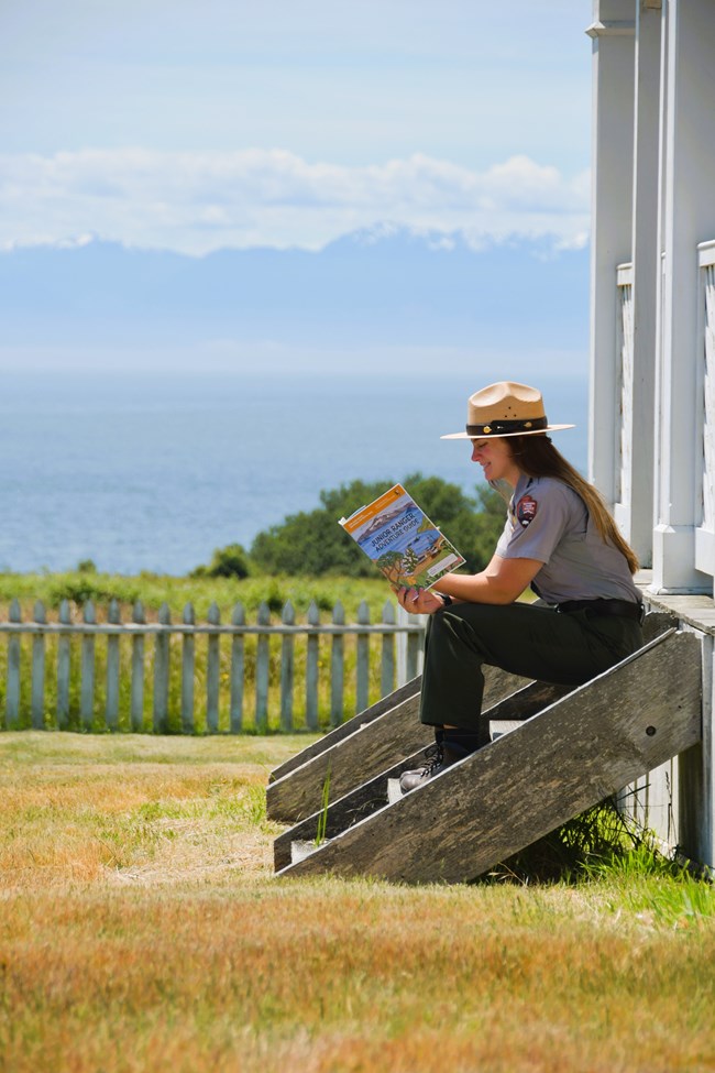 A Park Ranger sitting on porch stairs while reading the Junior Ranger booklet.