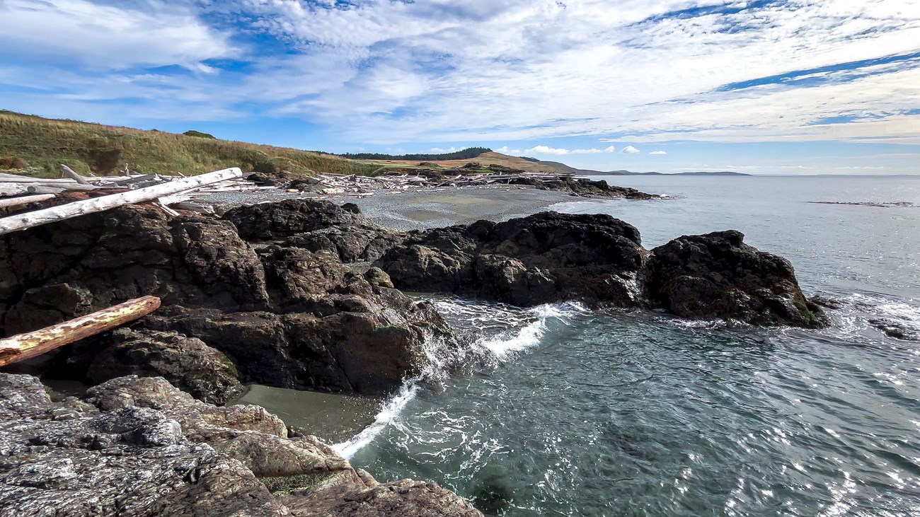 A rocky shoreline with a grassy hill in the background