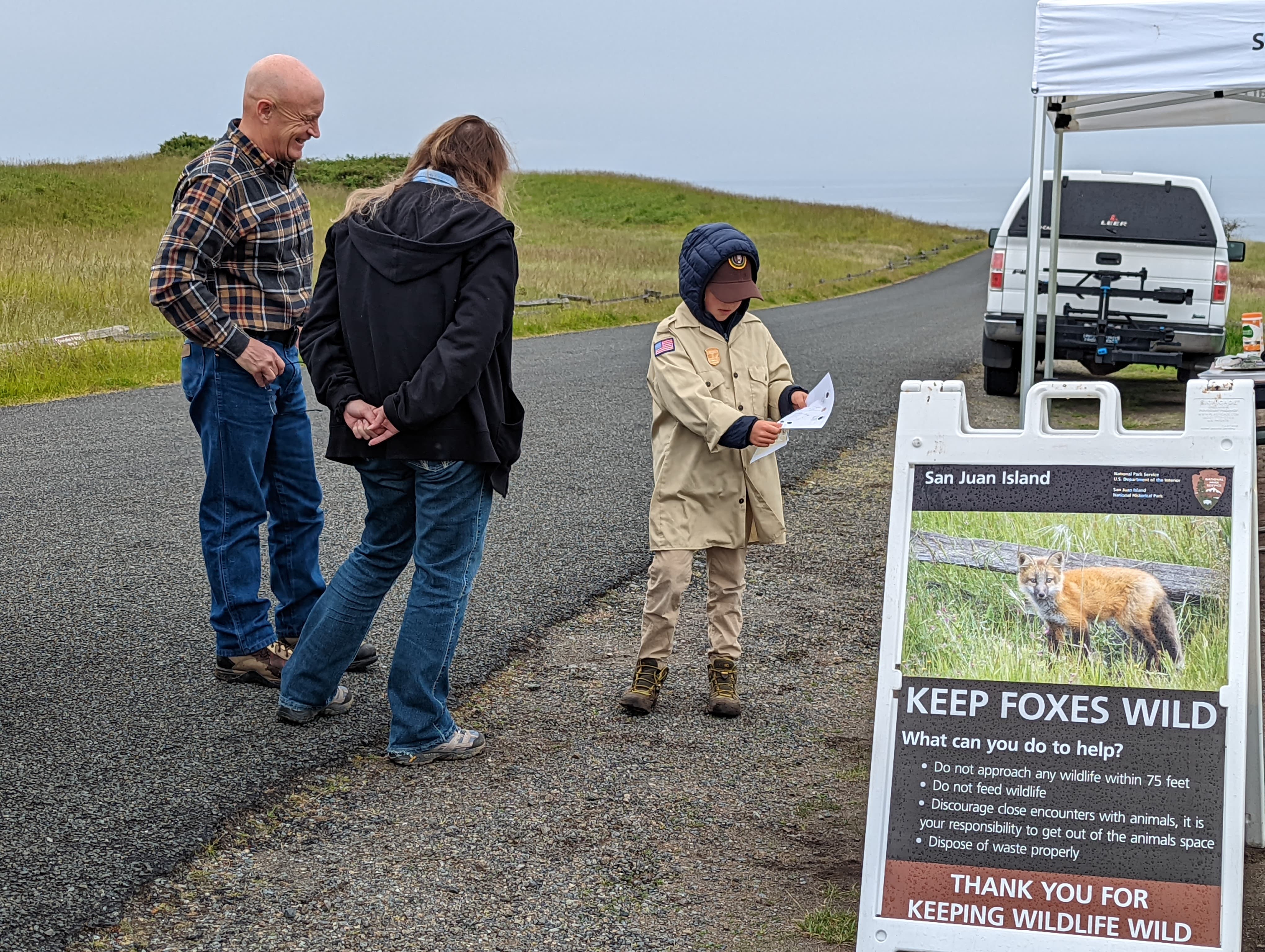 a young boy hands out pamphlets to visitors in front of a placard