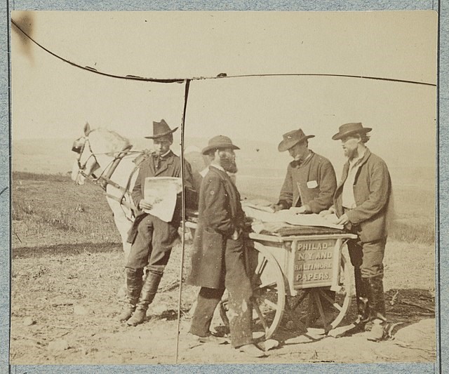 photograph of two men purchasing newspapers from a newsboy