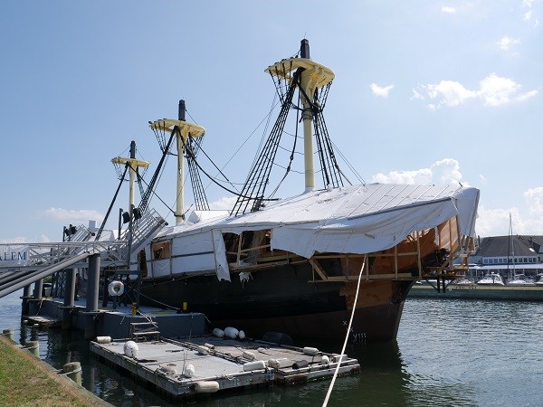 A wooden ship docked at a wharf with construction ongoing.