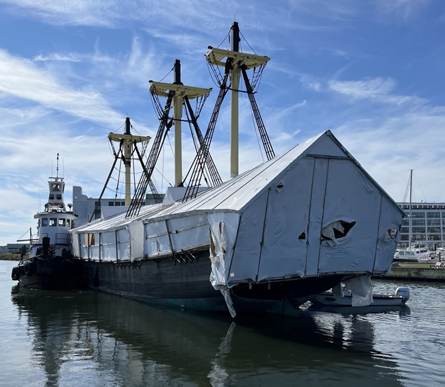 A tug boat helps navigate a large wooden ship in a harbor