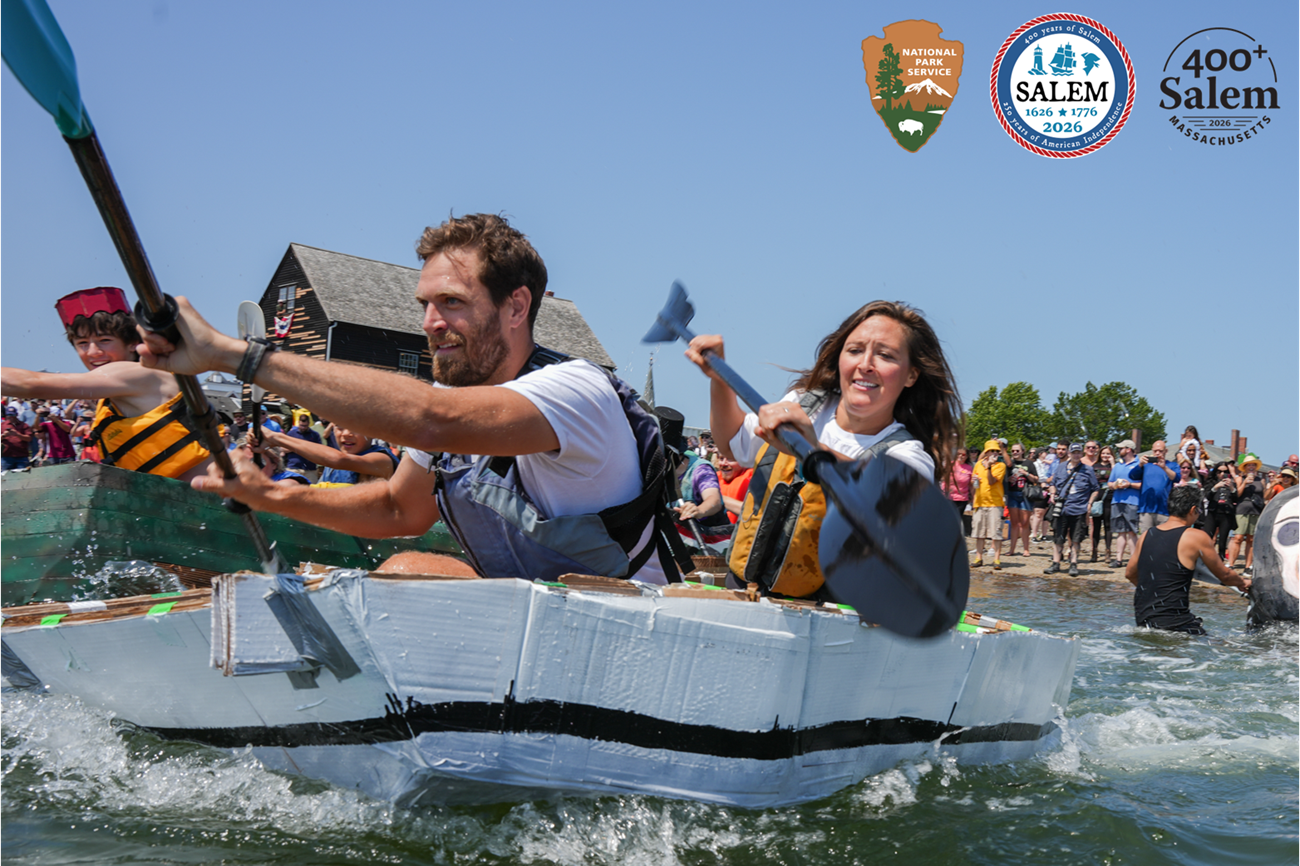 A couple paddles a boat made of cardboard for a fun race in the harbor.
