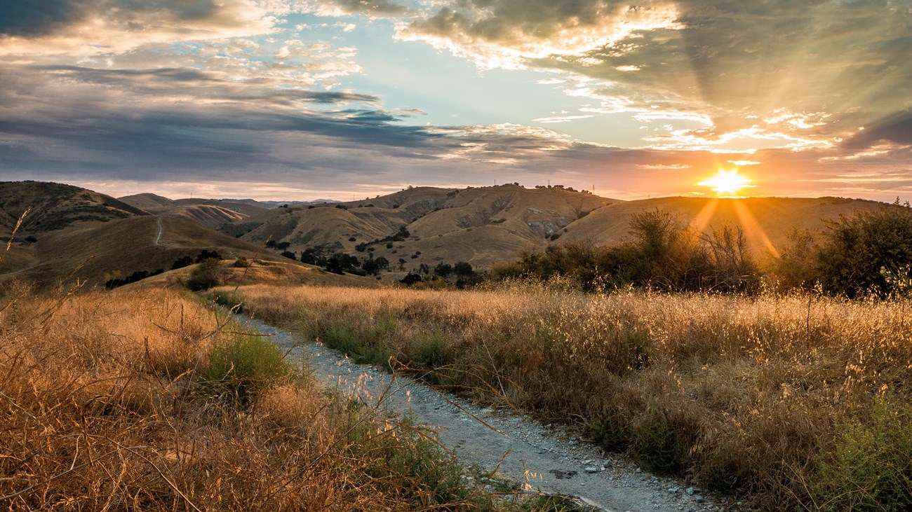 a colorful sunset above a mountainous terrain and dirt trail