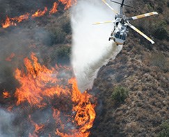 A fire helicopter drops water on a large fire.