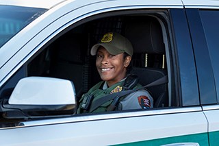 Uniformed ranger smiling in patrol vehicle.