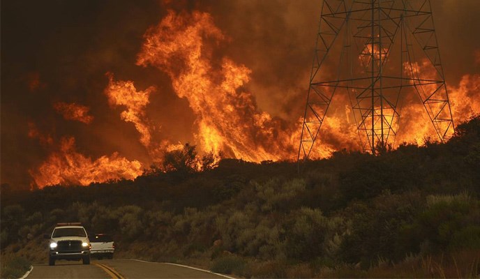Wildfire approaching transmission lines with two trucks in foreground