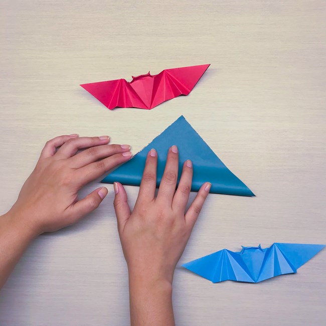 Hands fold a square piece of paper into a triangle shape.