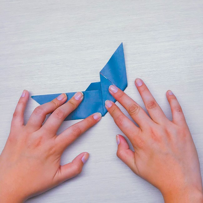 Hands folding the right side of the paper upwards, following the central crease.