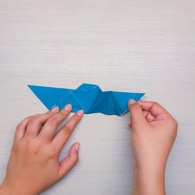 Right hands unfolding the right wing to display the four alternating creases that make up the wing.