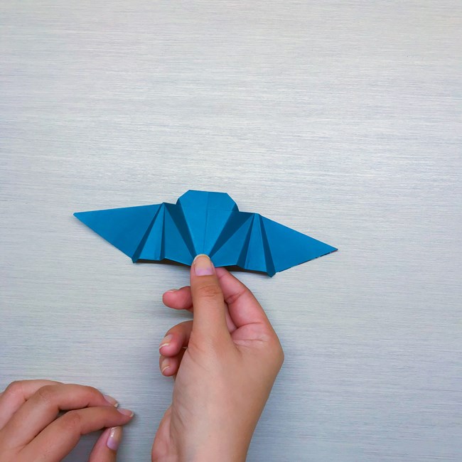 One hands holding the bottom of the origami bat after it has been flipped over.