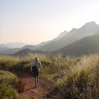 A late-afternoon hiker walks along a trail as mountains fade into the horizon