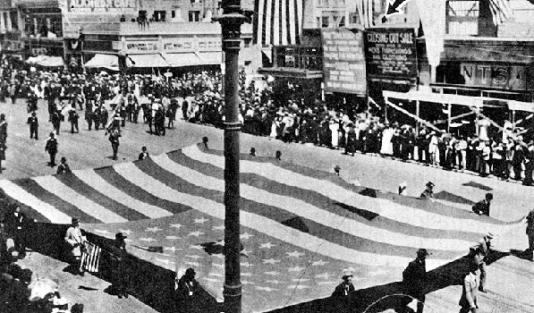 many people parading on a street holding a large American flag
